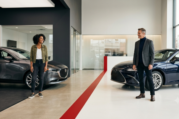 Two figures in a modern car dealership showroom: two distinct buyers on either side and a red accent line across the floor.